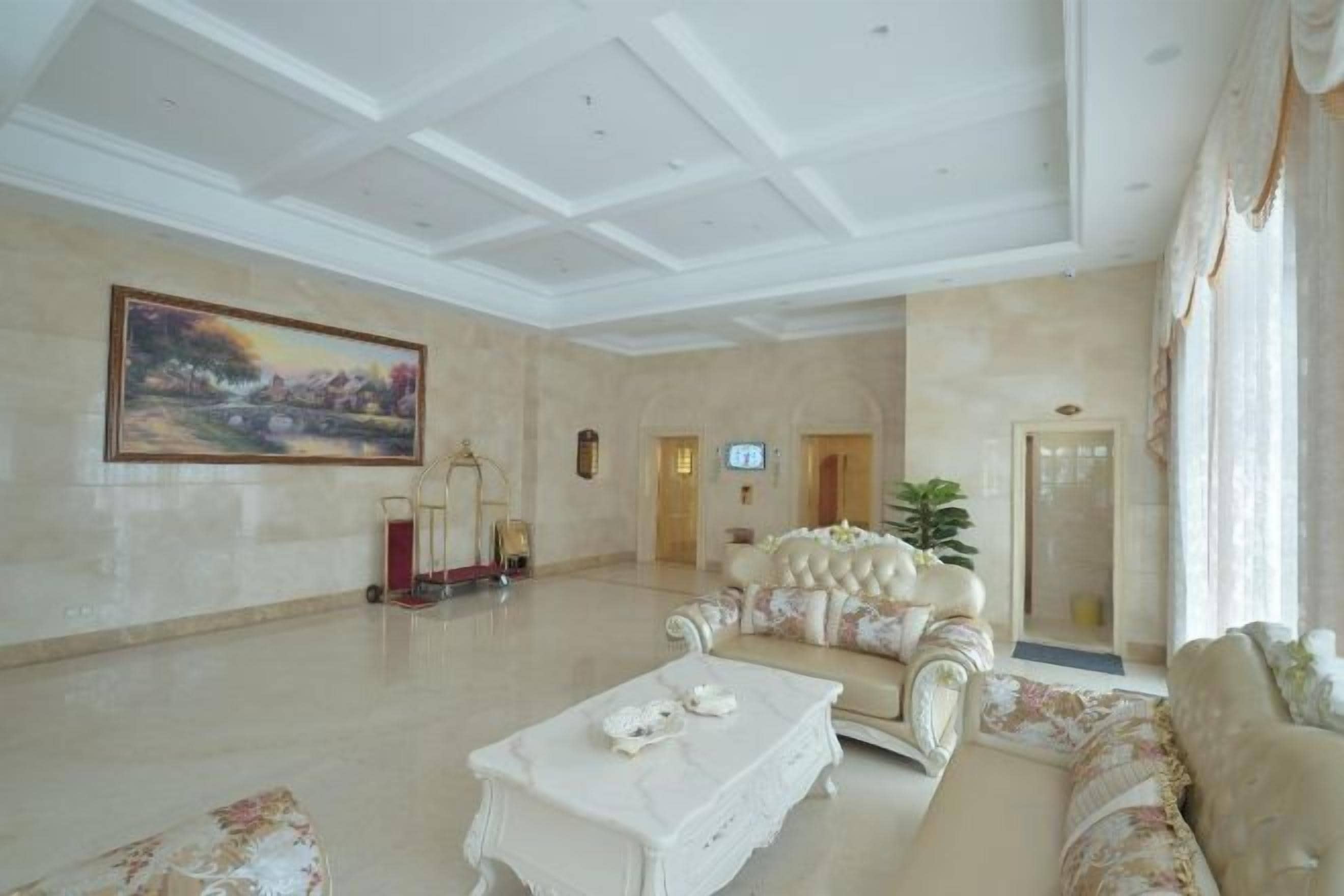 A spacious living room with a high ceiling, a large painting, a sofa, a coffee table, and a television.