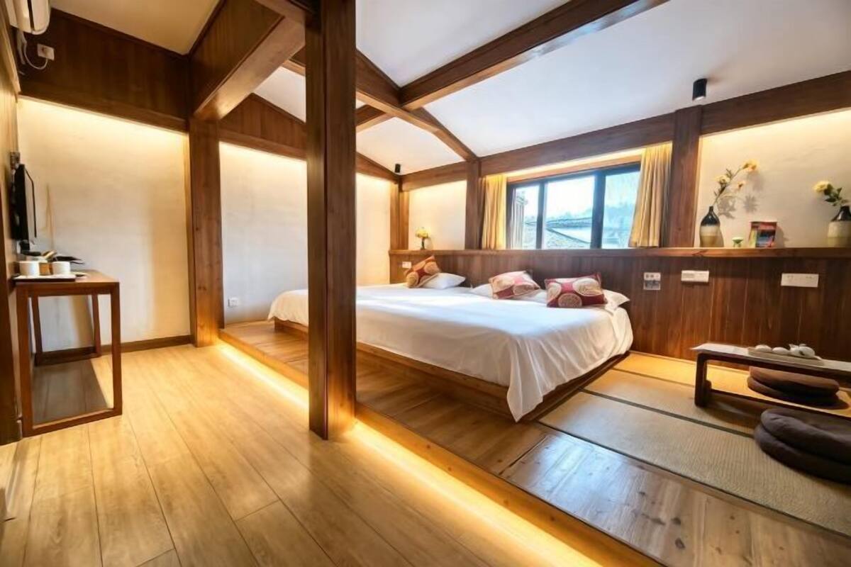 Une chambre à coucher avec un lit, un plancher en bois, une fenêtre avec des rideaux et une table de chevet.