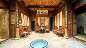 A traditional wooden interior with a central seating area, wooden pillars with calligraphy, and a large blue and white vase in the foreground.