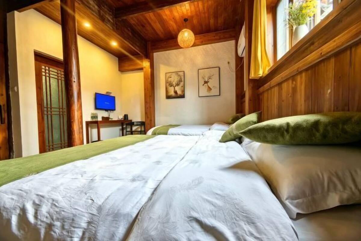 Une chambre avec deux lits, un plafond en bois, une télévision et des œuvres d’art accrochées au mur.