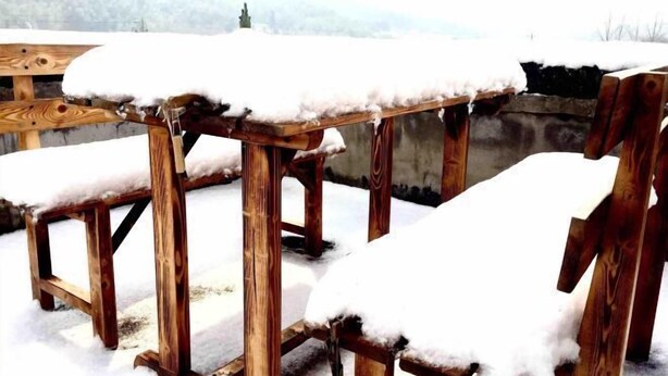 A wooden outdoor seating area with snow-covered chairs and a table.