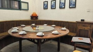 A round dining table with white plates and chopsticks, surrounded by wooden chairs.