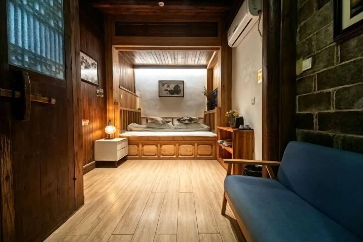 Une pièce confortable avec un lit, un canapé bleu, une petite table et une étagère fixée au mur.