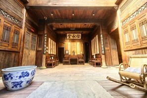 Ein traditionelles Holzinnenambiente mit einem zentralen Tisch und Stühlen, einer großen, blau-weißen Keramikschüssel und einem Holzschlitten.