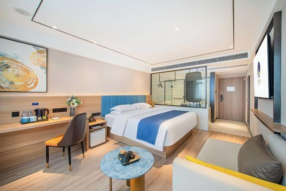 A modern hotel room with a large bed, a desk, a chair, a small round table, and a sofa.