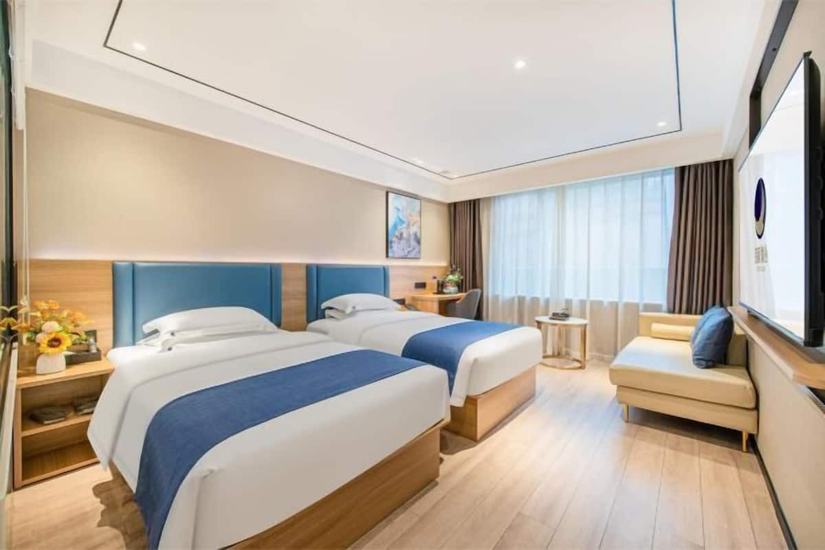 A hotel room with two beds, a sofa, a small table, and a large window with curtains.