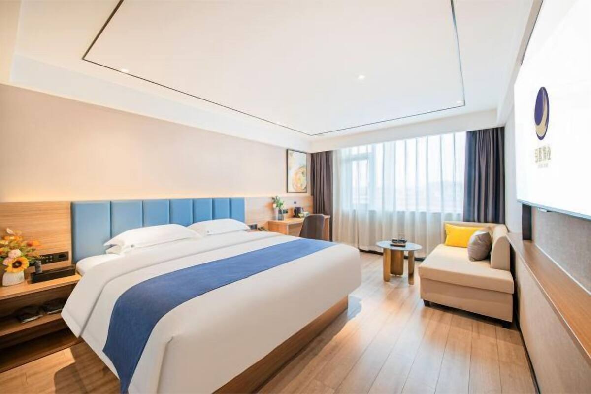 A modern hotel room with a large bed, a small sofa, a desk, and a window with curtains.