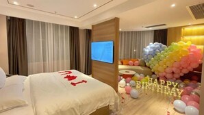 A hotel room with a bed, curtains, a TV, and a colorful balloon decoration. - BIJIU HOTEL (Foshan)
