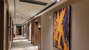 A hotel hallway with a patterned carpet, a large abstract painting on the wall, and a visible exit sign. - BIJIU HOTEL (Foshan)