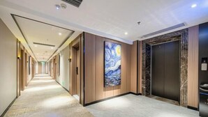 A hotel corridor with a long hallway, wooden panel walls, a large painting, marble flooring, and a modern elevator. - BIJIU HOTEL (Foshan)