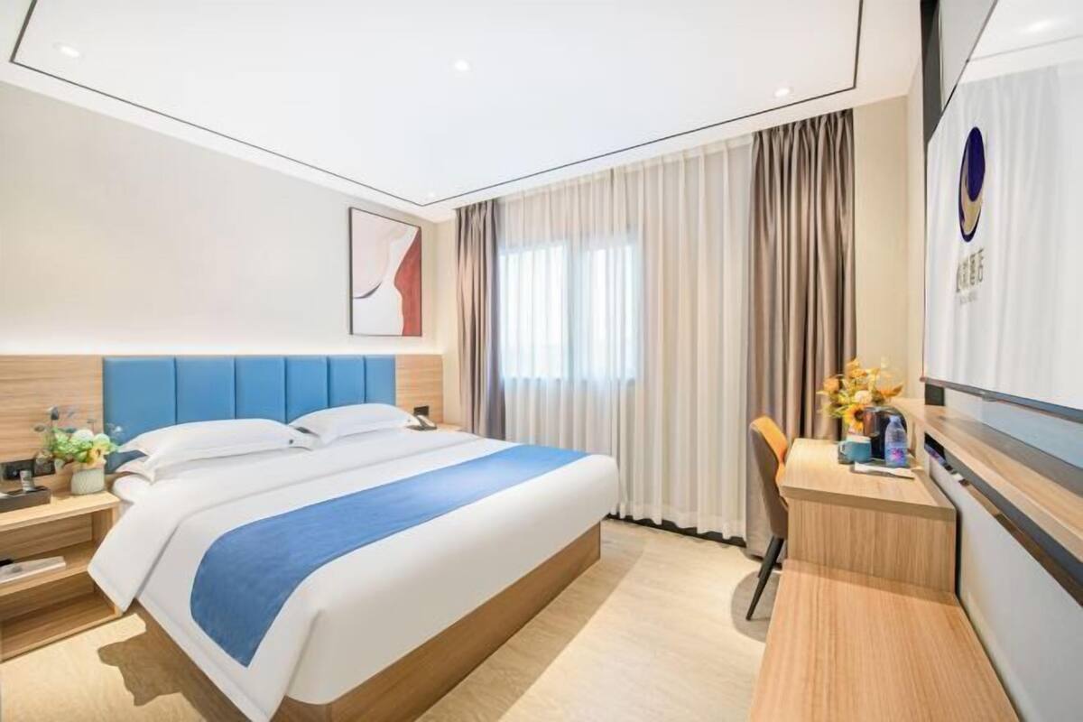 A hotel room with a bed, bedside table, and a desk with a chair.