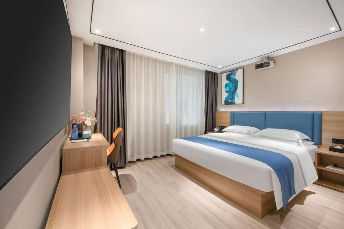 A modern hotel room with a bed, desk, chair, and a large window with curtains.