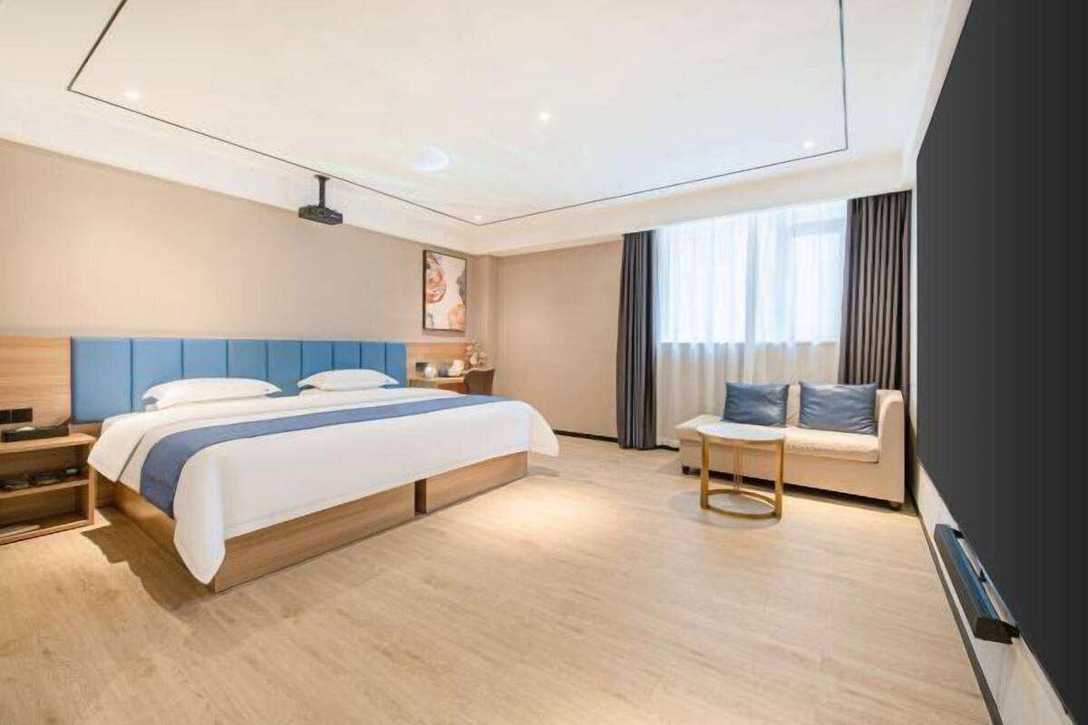 A modern hotel room with a large bed, bedside tables, a small sofa, and a ceiling projector.