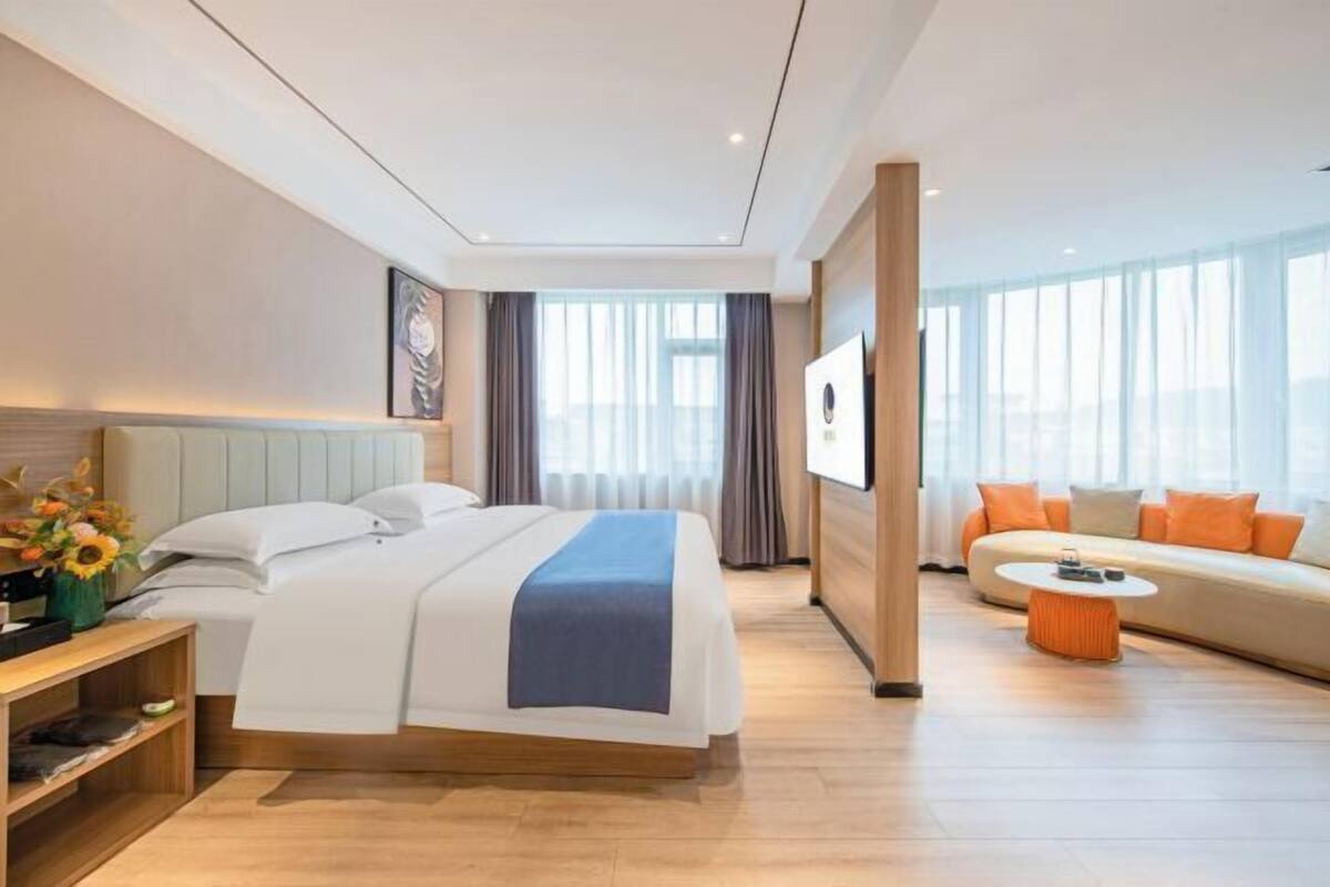 A hotel room with a bed, a sofa, a coffee table, a TV, and a window with curtains.