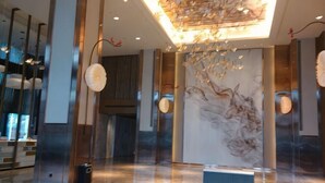 Un hall d’entrée avec un mur en marbre, un lustre moderne et un comptoir d’accueil.