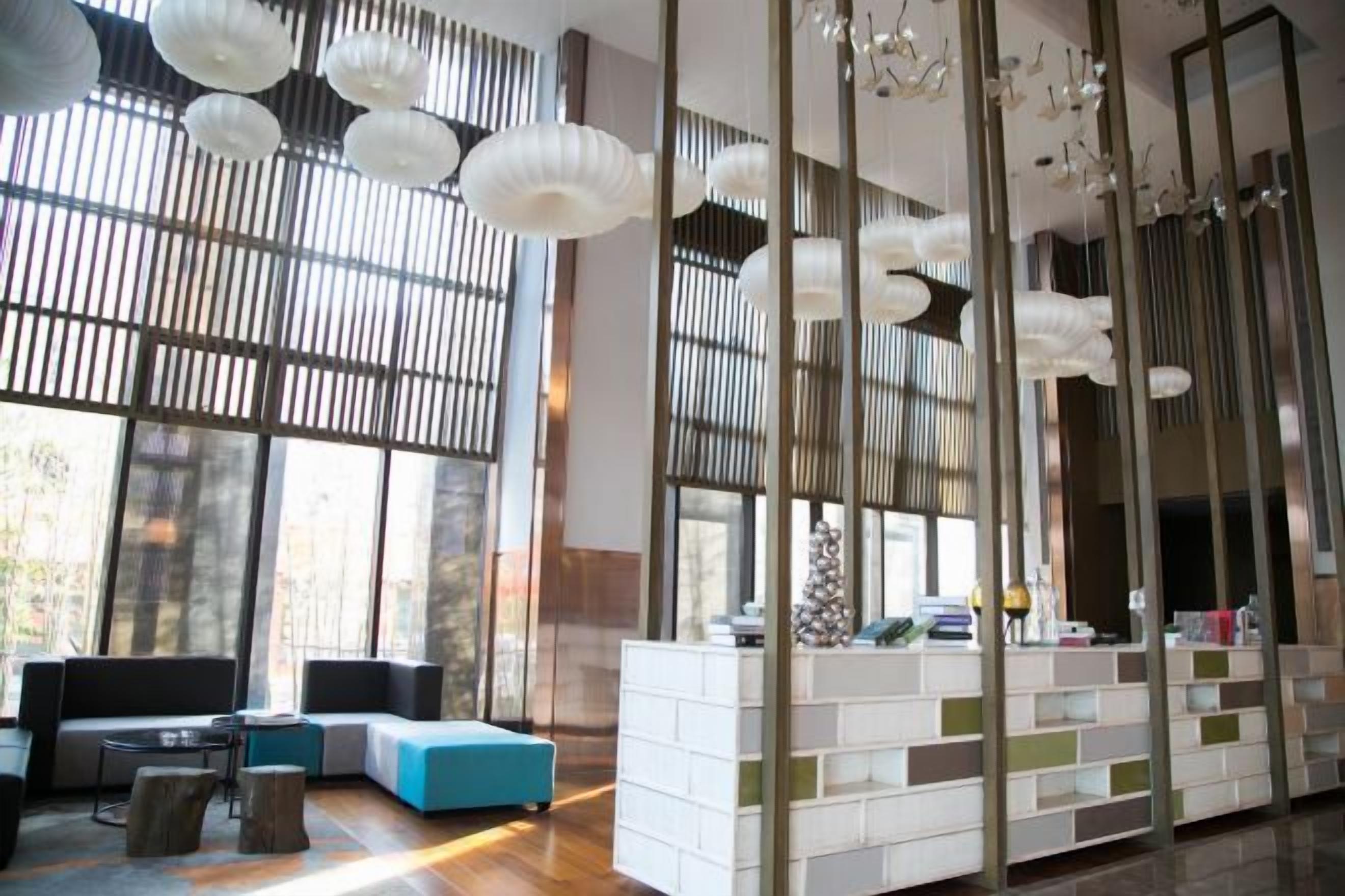 A modern hotel lobby with a seating area, a reception desk, and large windows.