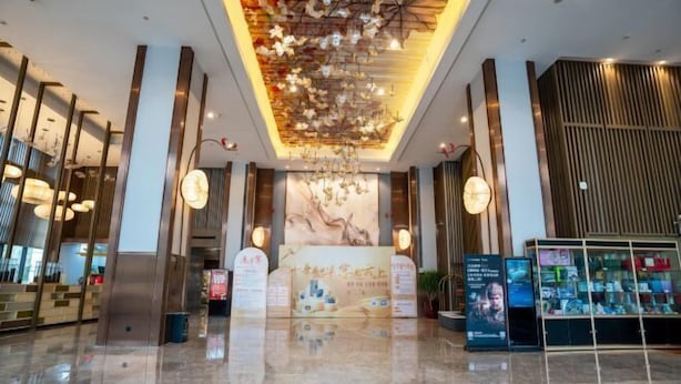 Un hall d’entrée moderne avec un comptoir d’accueil central, une grande fresque murale et une vitrine en verre contenant divers objets.