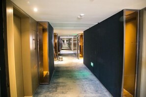 A hotel corridor with a carpeted floor, doors on both sides, and a visible emergency exit sign. - Yunshang City Impress Hotel (Wuxi)