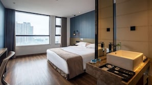 Une chambre d’hôtel moderne dotée d’un grand lit, d’un bureau, d’une salle de bain avec un grand lavabo et offrant une vue sur la ville.