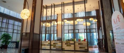 Un vestíbulo amplio con mostrador de recepción, ventanas grandes y luminarias modernas.