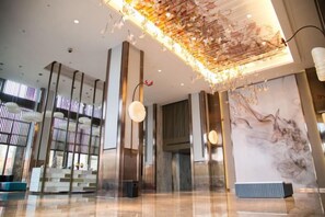 A modern lobby with a high ceiling, large windows, and a marble wall. - Yunshang City Impress Hotel (Wuxi)