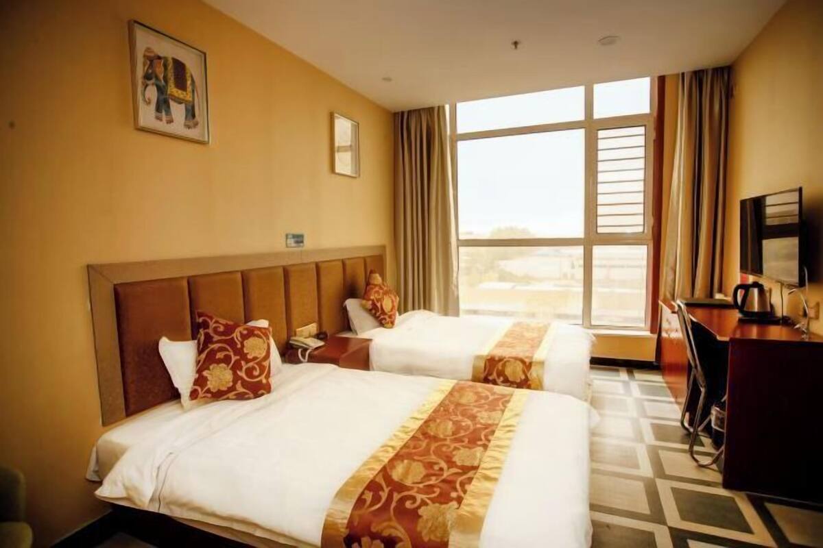 Habitación de hotel con dos camas, un escritorio, una silla y un ventanal grande.