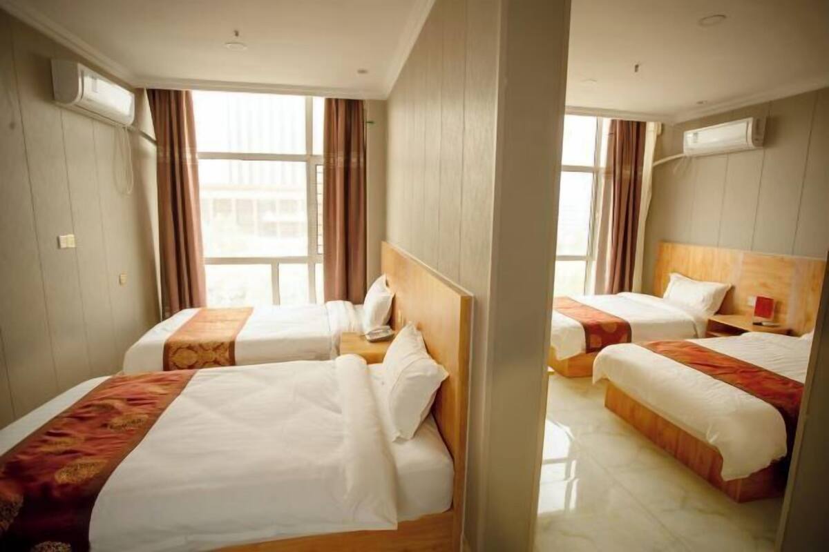 Habitación de hotel con dos camas, cabecero de madera, ventana con cortinas y un equipo de aire acondicionado.