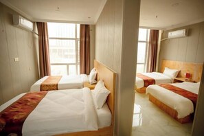 A hotel room with two beds, a wooden headboard, a window with curtains, and an air conditioning unit. - Seven Hotels (Yinan)