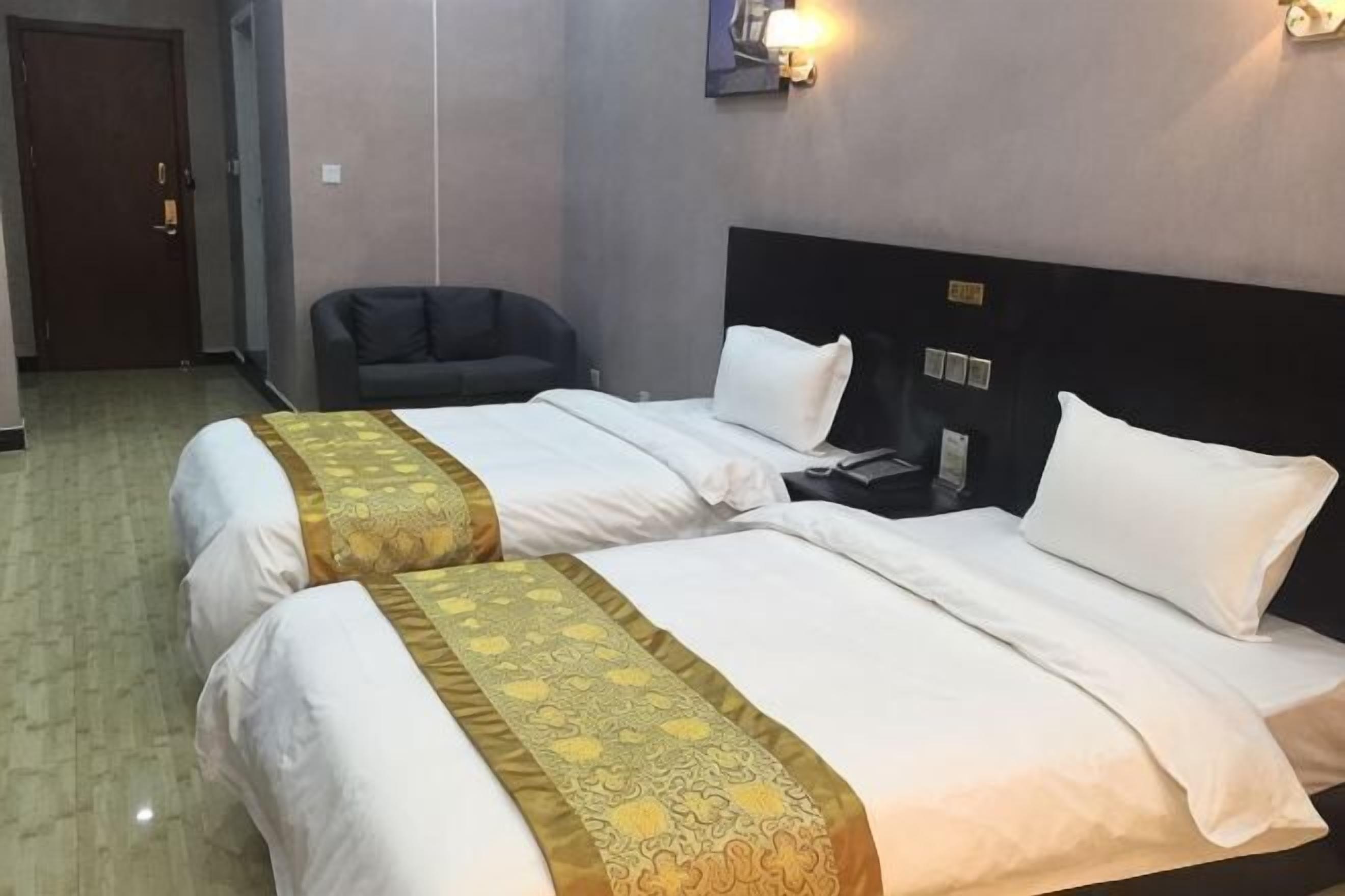 A hotel room with two beds, a sofa, a nightstand, and a wall-mounted light fixture.
