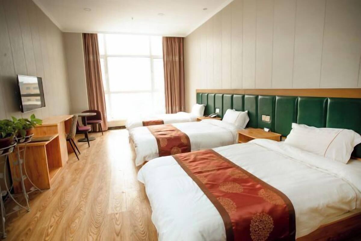 Una habitación de hotel con dos camas, un escritorio, una silla, un televisor y un ventanal amplio.