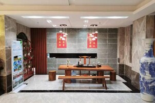 Un área de recepción con mostrador, un banco, un jarrón grande y una pared con pancartas rojas.