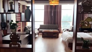 Una habitación con sofá, una mesa de centro y cama. Hay una ventana con cortinas, una planta y un jarrón decorativo.