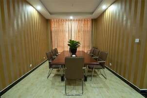 Un salón de conferencias con una mesa rectangular rodeada de sillas, una planta en maceta y una pared a rayas.