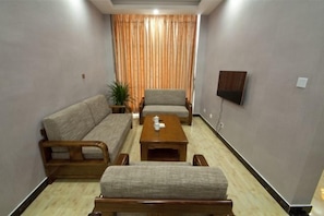 Una sala de estar con sofá, sillón y reposapiés, una mesa de centro, una planta en maceta y un televisor de pantalla plana montado en la pared.