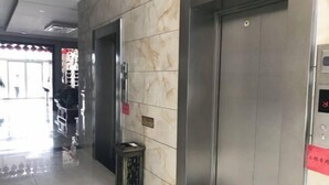 An elevator in a hotel lobby with a marble wall and a small trash bin beside it. - Seven Hotels (Yinan)