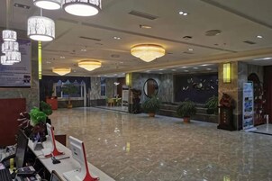 Un vestíbulo de hotel con mostrador de recepción, zona de estar y plantas decorativas.