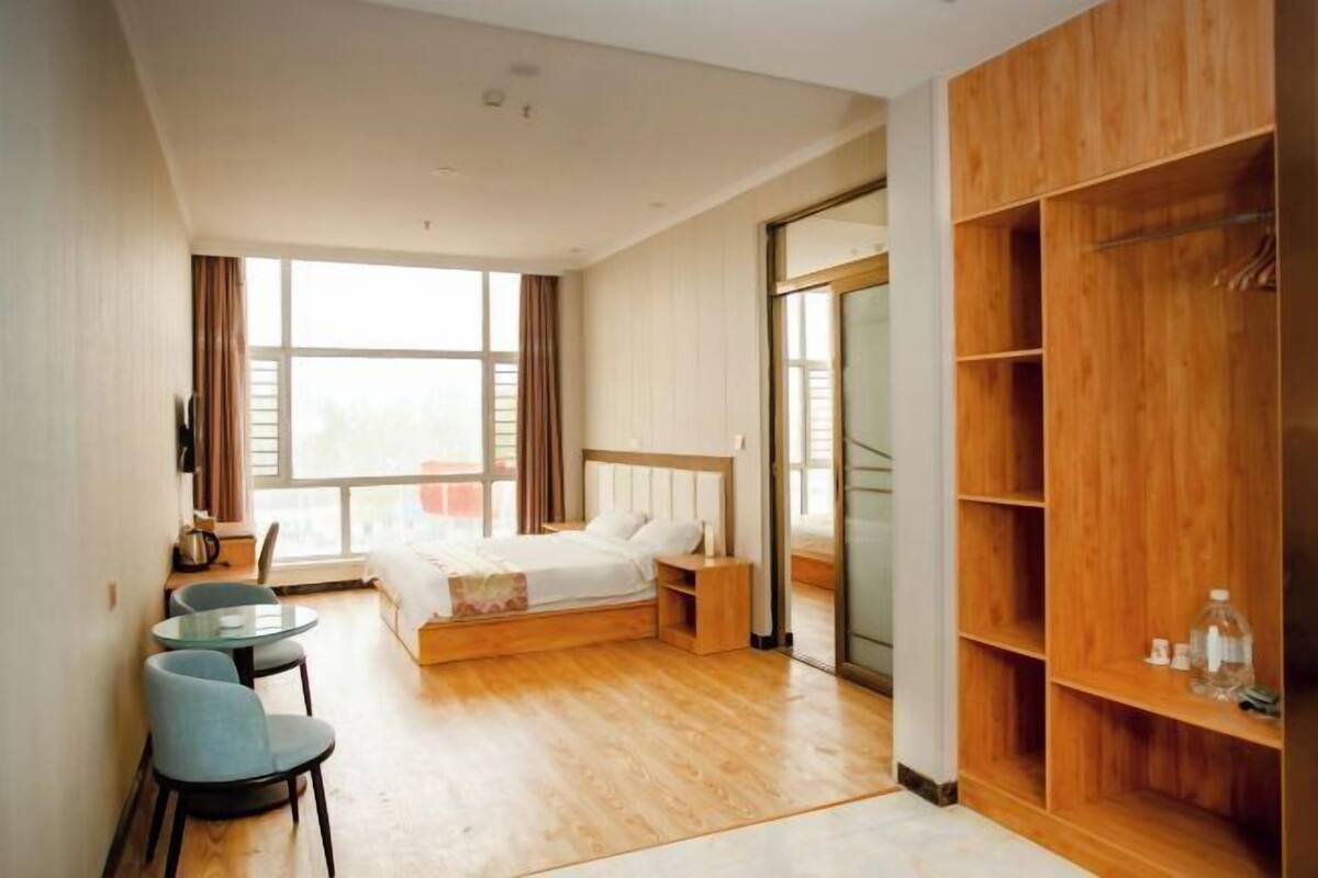 Una habitación de hotel moderna con cama, escritorio, sillas, armario y un amplio ventanal.