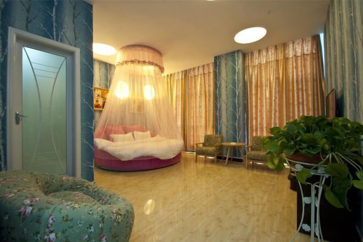 Un dormitorio con cama redonda, una mesita, una silla y una planta en maceta.