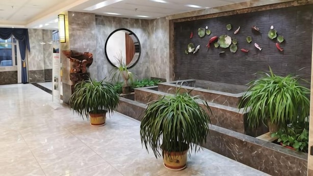 Vestíbulo con suelo de mármol, plantas en macetas, mostrador de recepción, espejo adosado a la pared y una pared decorativa con motivos de frutas.