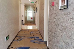 Un pasillo de hotel con alfombra estampada, una pared de ladrillo en un lateral y un cuadro enmarcado en la pared.