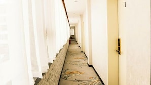 Een hotelgang met een tapijten vloer, witte muren en een deur aan de rechterkant.