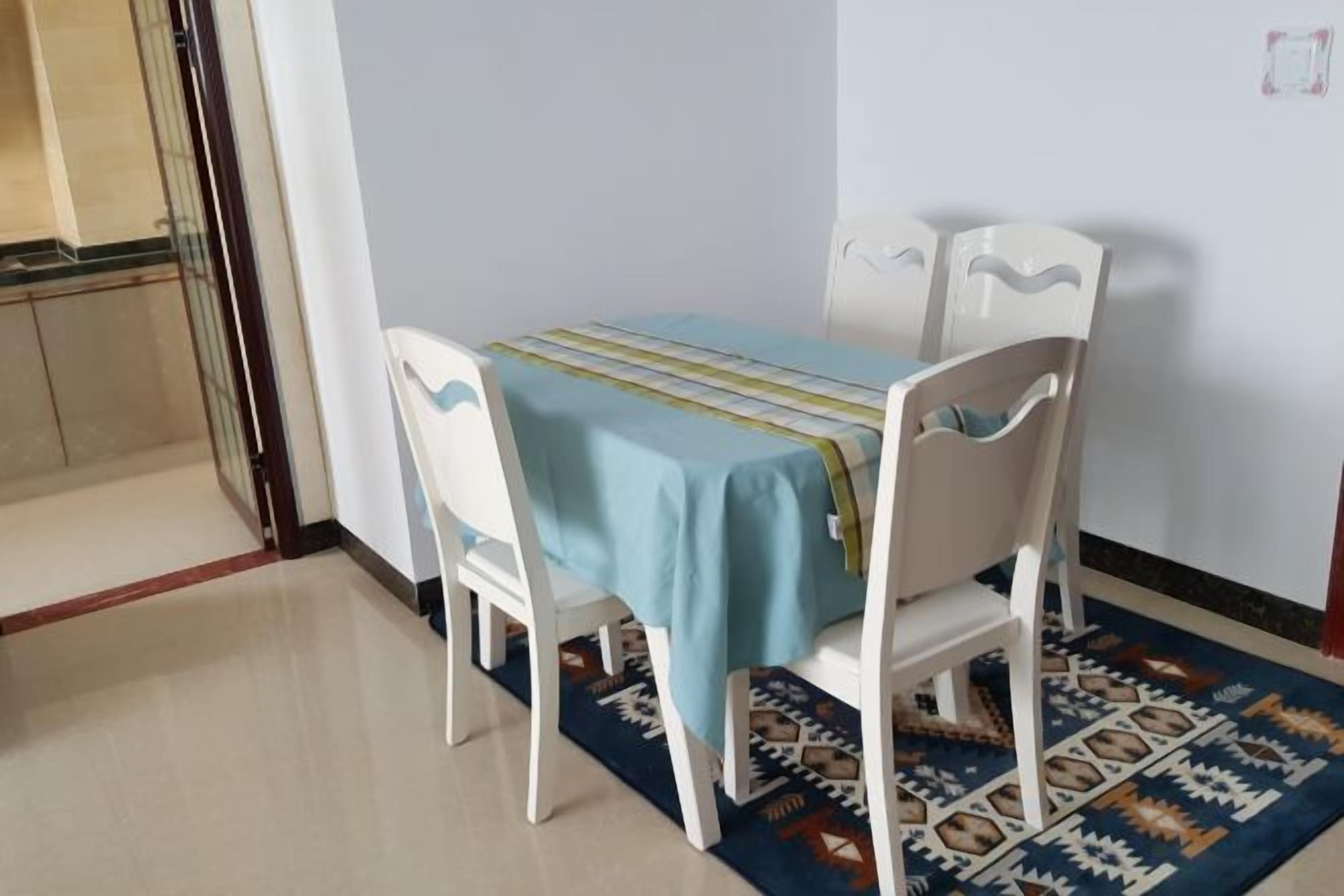 Un comedor con una mesa, sillas, un tapete estampado y una pared blanca.