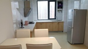 A modern kitchen with a dining table and chairs, a refrigerator, and a window with a view of buildings.