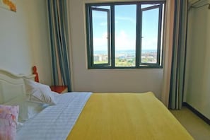 Een slaapkamer met een bed, een raam met gordijnen en uitzicht op een stadsbeeld.
