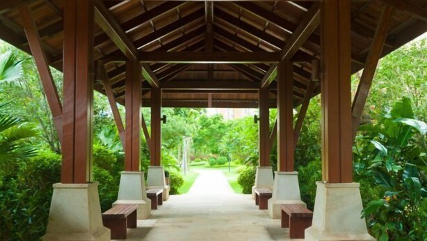 A covered walkway with benches, surrounded by lush greenery.