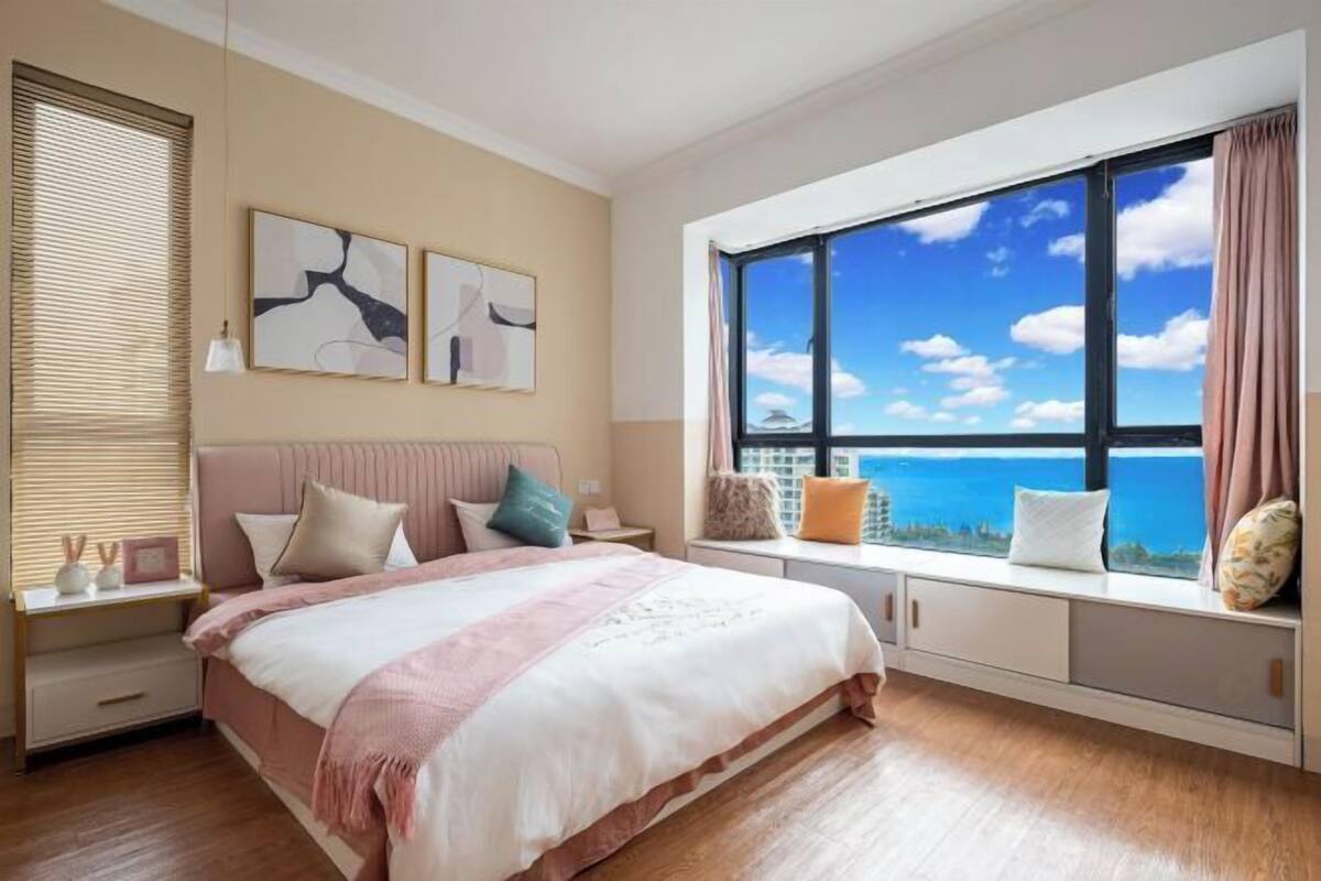 Een slaapkamer met een groot bed, een vensterbank met kussens en kunst aan de muur.