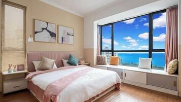 Un dormitorio con una cama grande, un rincón con ventanilla y cojines, y una obra de arte en la pared.