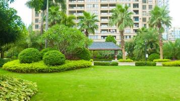 Un jardín bien cuidado con un pabellón, palmeras y un edificio de varios pisos al fondo.
