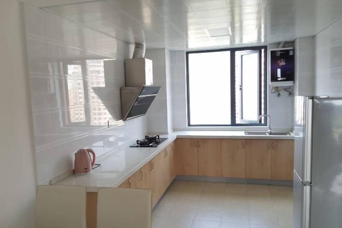Een moderne keuken met witte kastjes, een roestvrijstalen koelkast en een raam dat voor natuurlijk licht zorgt.