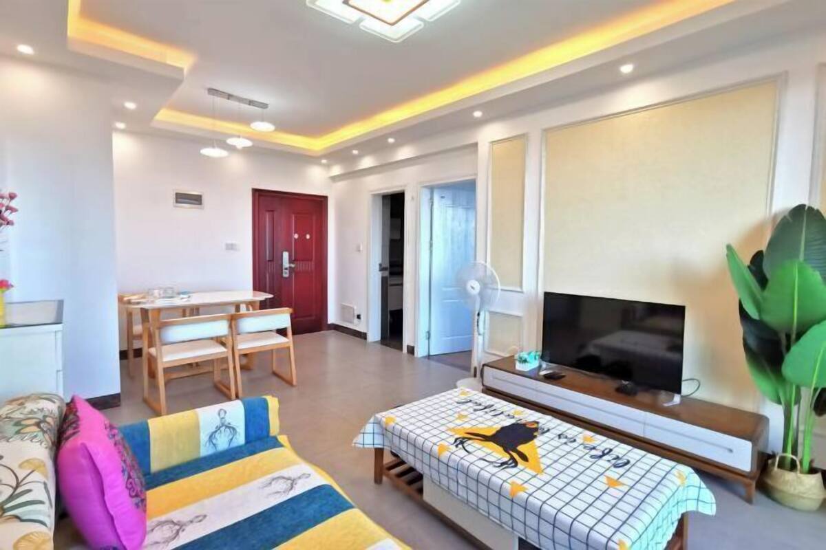 Uma sala de estar moderna com um sofá, uma mesa de jantar com cadeiras, uma TV e uma planta grande.
